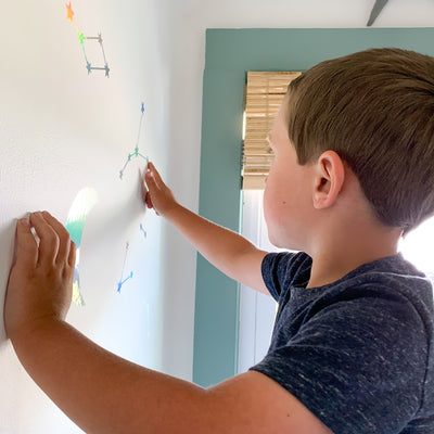 A little boy adding Constellations & Moons wall decals from Tempaper to his wall.