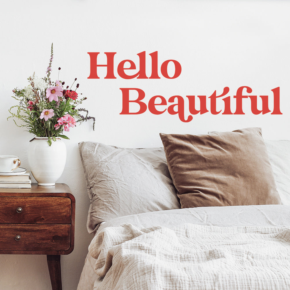 A bed and wood nightstand with flowers showing off the Hello Beautiful wall decal from Tempaper.
