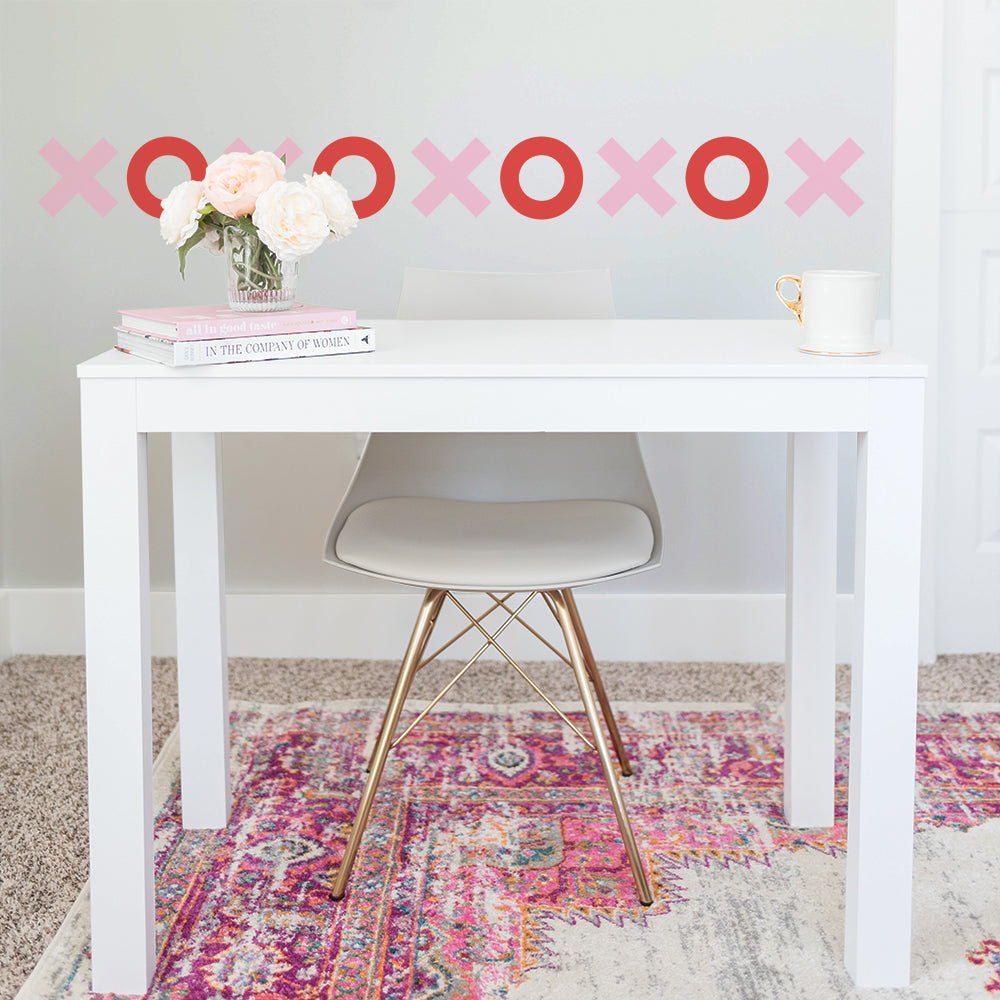 Pink and red Tic Tac Toe wall decals from Tempaper lined up on a wall behind a white desk and chair sitting on a faded pink rug.