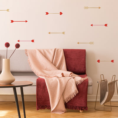 A living room with a sofa with pink and red blankets draped on it, a magazine holder, a coffee table, and Tempaper's Cupid's Arrow wall decals on the wall. 