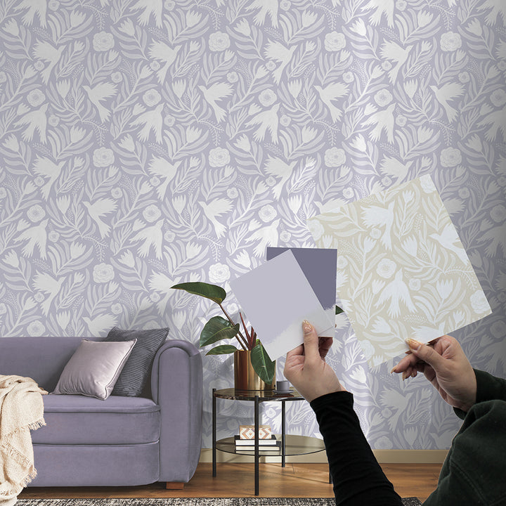 Image of a customer holding up an existing Tempaper wallpaper print alongside two paint swatches they are considering to recolor the print. Next to them is a room featuring a feature wall showcasing the newly printed wallpaper in the updated colorway, created by Tempaper.