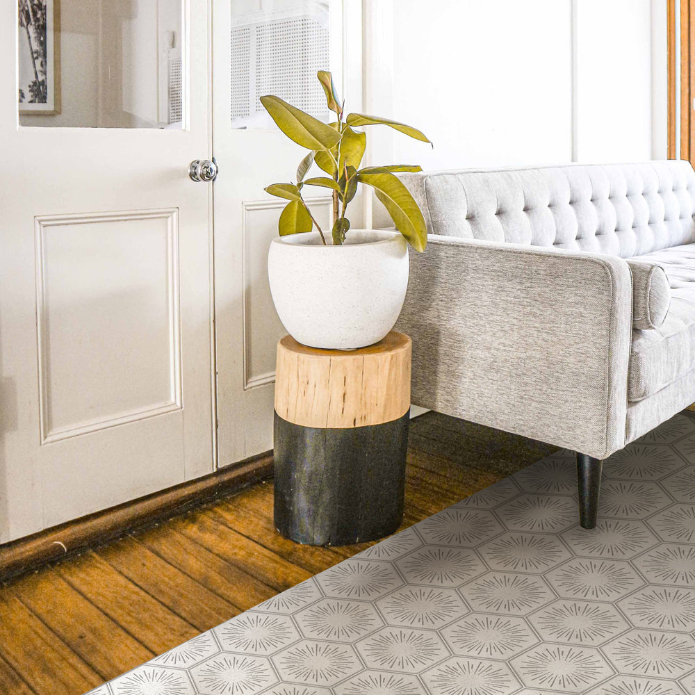 Tempaper's Hello Sunshine Vinyl rug shown in grey underneath a grey couch in a living room.