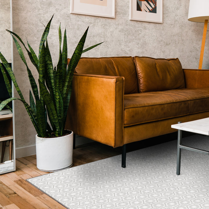 Tempaper's Hello Sunshine Vinyl rug shown in grey underneath a white coffee table and brown couch.