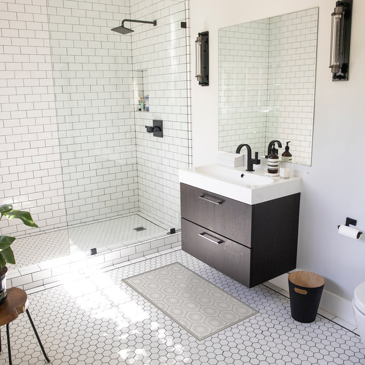 Tempaper's Hello Sunshine Vinyl rug shown in grey in front of a white sink in a bathroom.