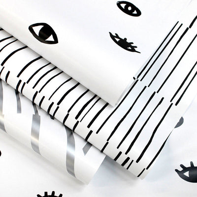 A roll of black and white Eye See You removable wallpaper resting with other wallpaper designs from Tempaper.#color_white-and-black-eyes