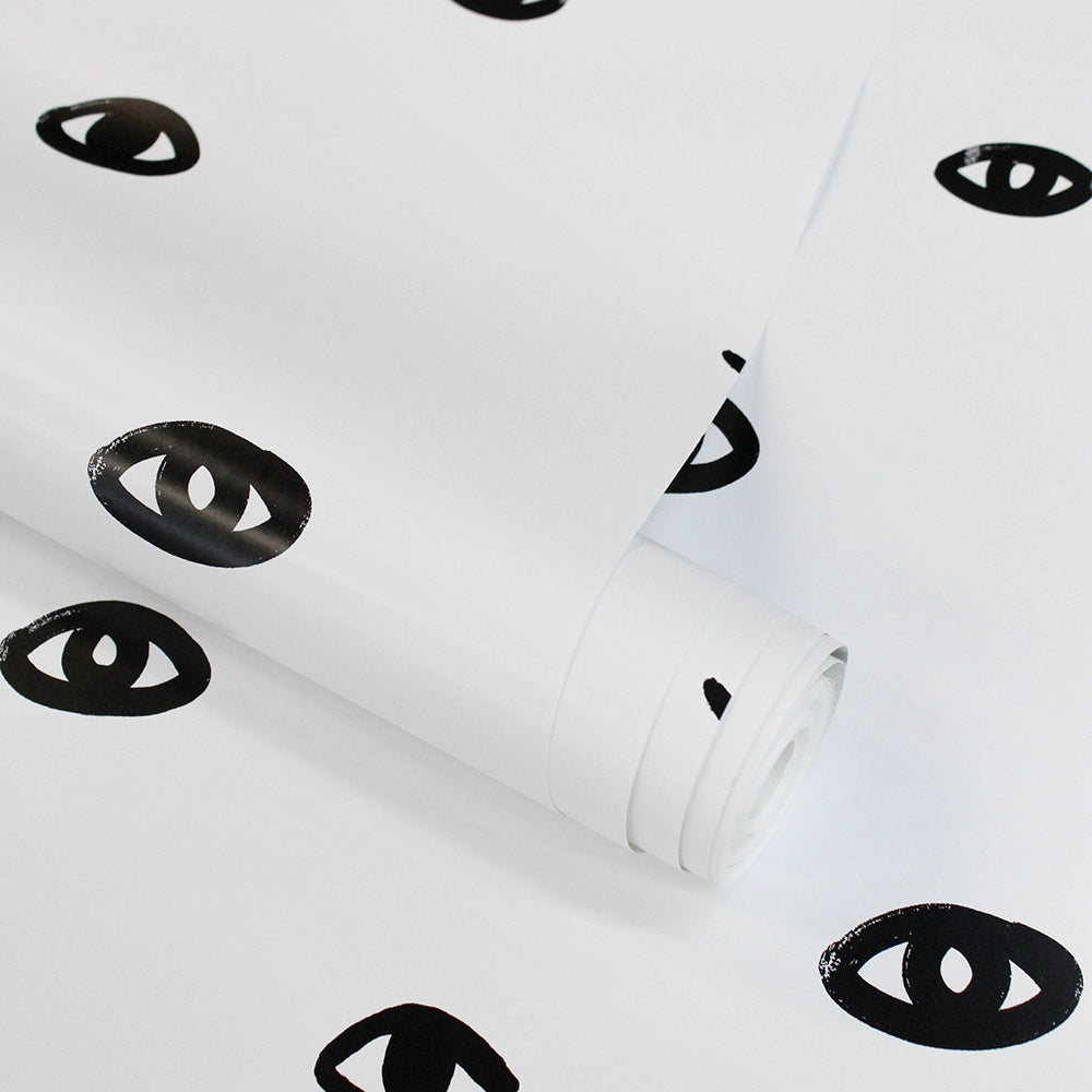 A roll of Tempaper's black and white Eye See You removable wallpaper resting on another panel with the same design.#color_white-and-black-eyes