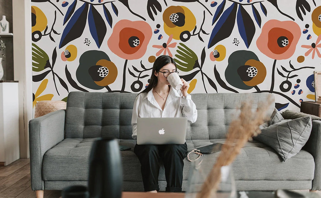 Image of a girl sitting on a couch with her laptop drinking coffee in front of a Tempaper custom mural