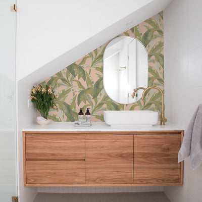 A white sink and wood vanity in front of Tempaper's Banana Leaf Peel And Stick Wallpaper.