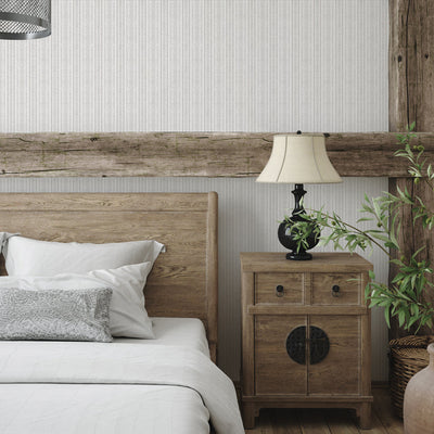 Batik Stripe Removable Wallpaper - A bed with a wood headboard and wood nightstand in a bedroom featuring Batik Stripe Peel And Stick Wallpaper in french grey | Tempaper#color_french-grey