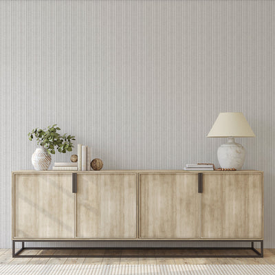 Batik Stripe Removable Wallpaper - A wood sideboard with a vase and lamp on top in front of a wall featuring Batik Stripe Peel And Stick Wallpaper in french grey | Tempaper#color_french-grey