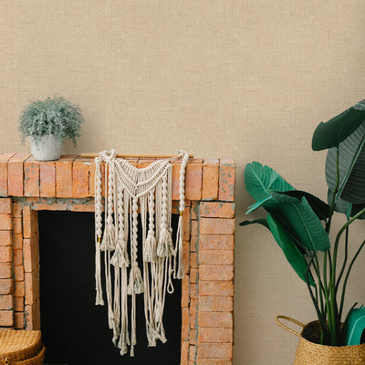 Burlap Removable Wallpaper - A brick fireplace and a plant in a room featuring Burlap Peel And Stick Wallpaper in natural burlap | Tempaper#color_natural-burlap