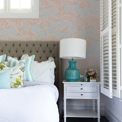 Flamingo wallpaper in a pastel colorway on the wall behind a fabric headboard #color_pastel-pink-and-blue