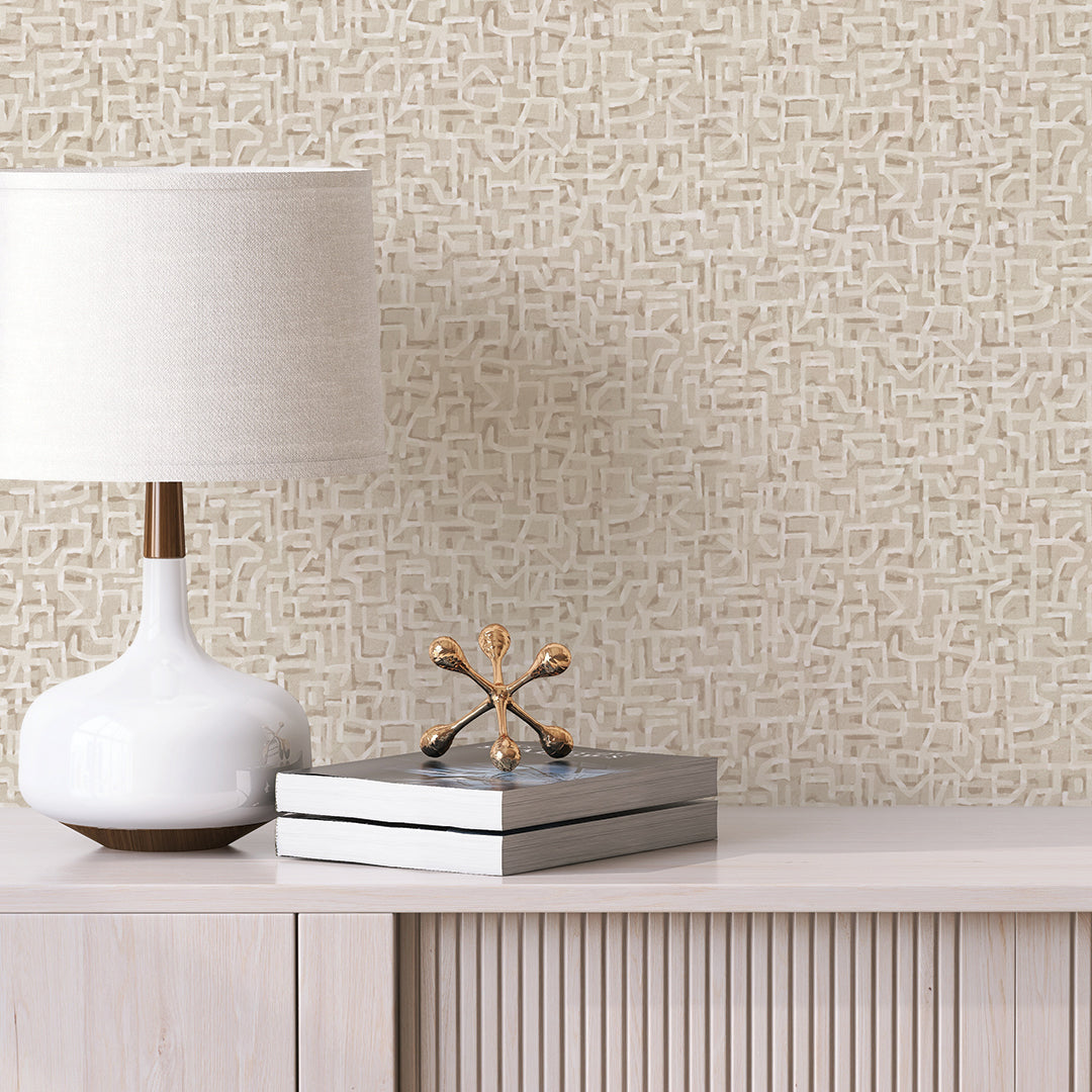 Glyph Geo Non-Pasted Wallpaper - A wood dresser with a white lamp and books in front of Glyph Geo Unpasted Wallpaper in fawn geo | Tempaper#color_fawn-geo