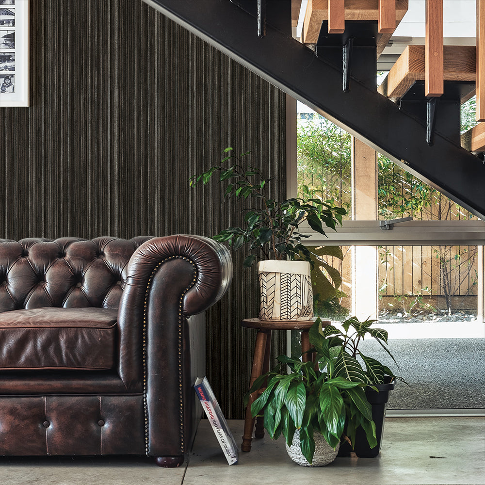 Faux Grasscloth Removable Wallpaper - A brown leather couch and plants underneath a staircase in a room featuring Faux Grasscloth Peel And Stick Wallpaper in textured black linen | Tempaper#color_textured-black-linen