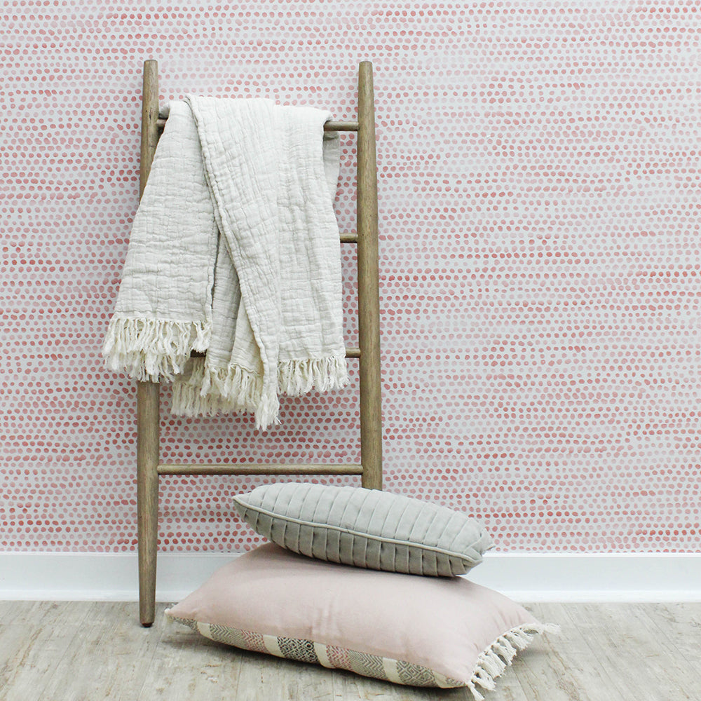 Moire Dots Removable Wallpaper - A wood ladder and pillows in front of a wall featuring Tempaper's Moire Dots Peel And Stick Wallpaper in coral dots | Tempaper#color_coral-dots