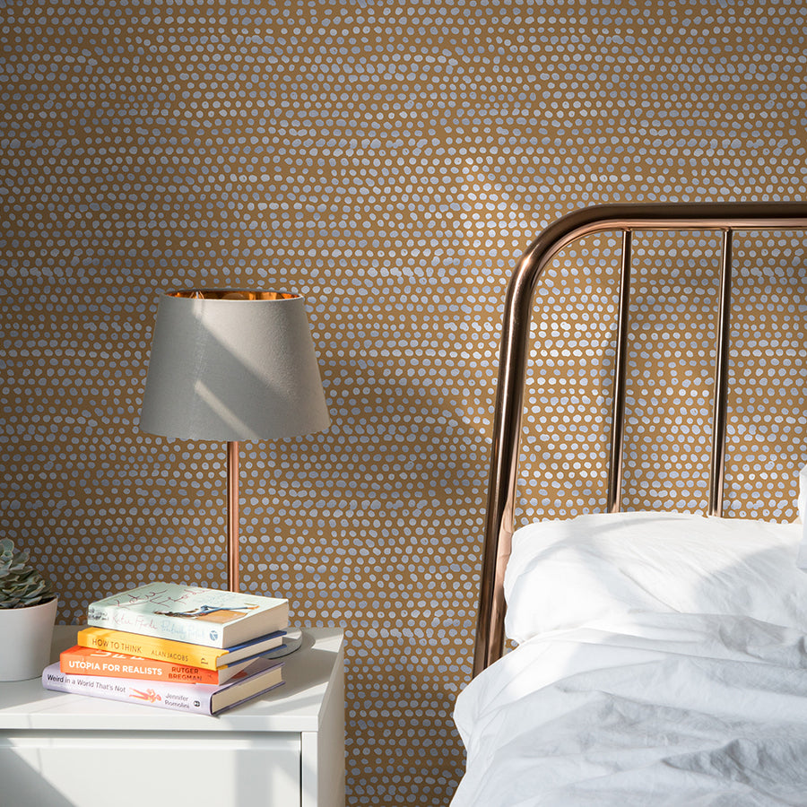 Moire Dots Removable Wallpaper - A bedroom with a bed and white nightstand in front of a wall featuring Tempaper's Moire Dots Peel And Stick Wallpaper in toasted turmeric dots | Tempaper#color_toasted-turmeric-dots
