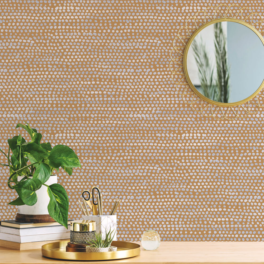 Moire Dots Removable Wallpaper - Three books, a plant, and gold mirror in front of a wall featuring Tempaper's Moire Dots Peel And Stick Wallpaper in toasted turmeric dots | Tempaper#color_toasted-turmeric-dots