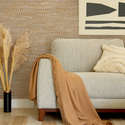 Moire Dots Removable Wallpaper - A grey couch with a tan throw blanket in front of a wall featuring Tempaper's Moire Dots Peel And Stick Wallpaper in toasted turmeric dots | Tempaper#color_toasted-turmeric-dots