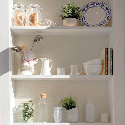 Tempaper's Geometric Patchwork Peel And Stick Wallpaper behind white shelves filled with white ceramic dishes.