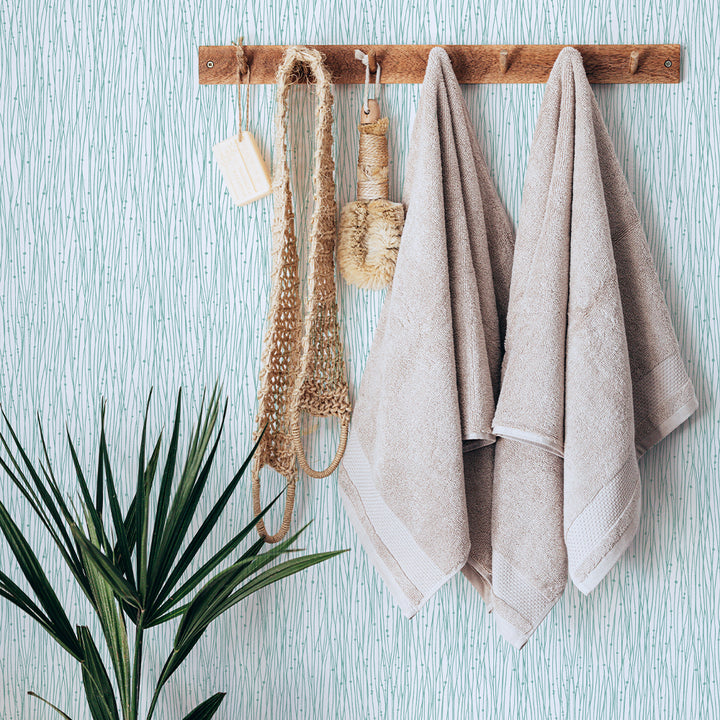 A wood towel hanger and plant in front of Tempaper's String of Pearls Temporary Wallpaper in green.