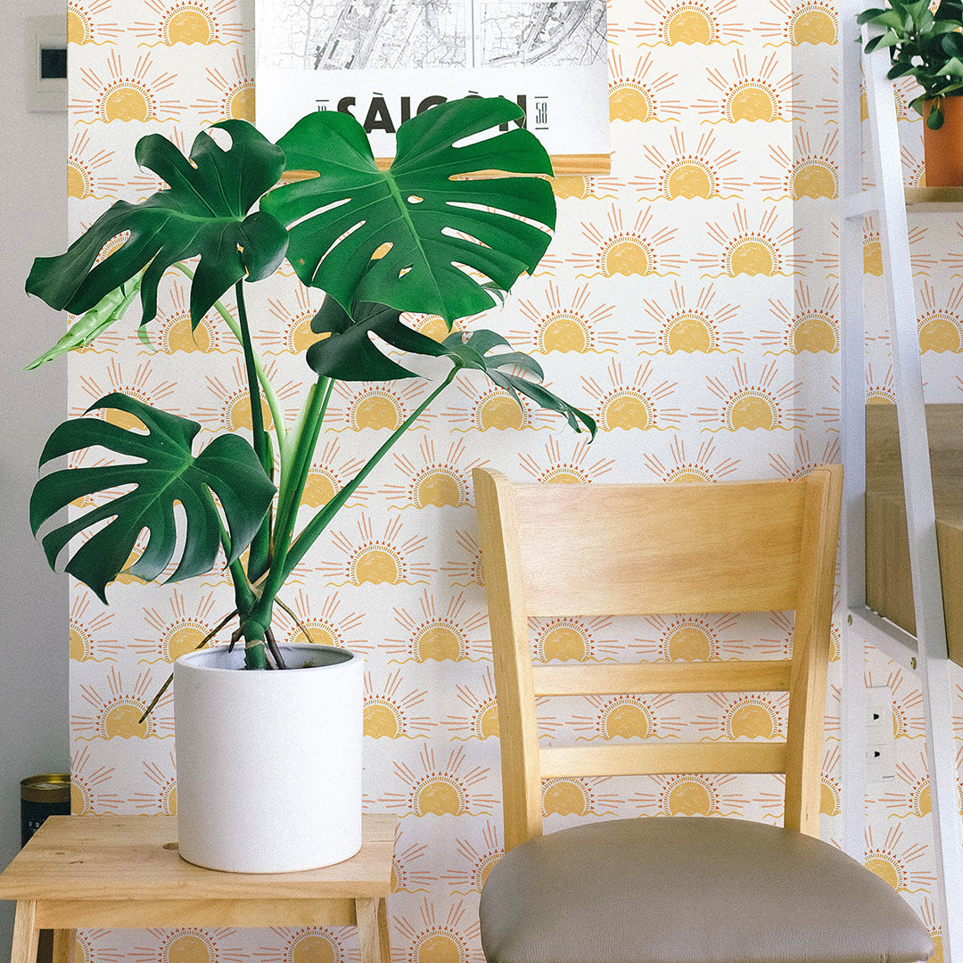 A plant and wood chair in front of Tempaper's Sun Peel And Stick Wallpaper.