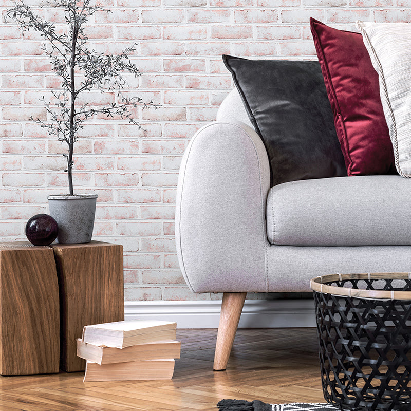 Tempaper's Whitewashed Brick Peel And Stick Wallpaper behind a plant and a grey couch with pillows.