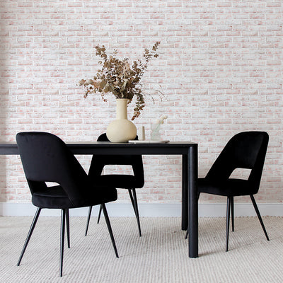 Tempaper's Whitewashed Brick Peel And Stick Wallpaper shown behind a black table with a plant on top and black chairs.