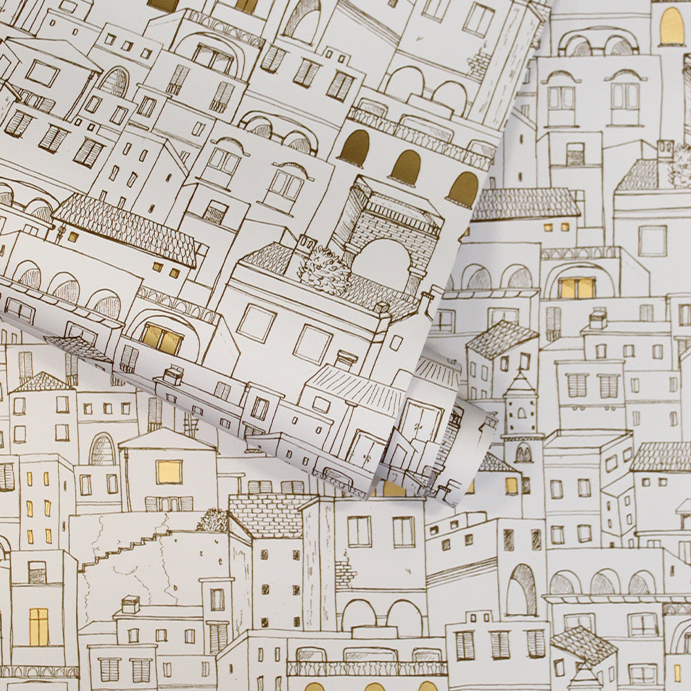 Amalfi WALLPAPER in a metallic gold and white color is shown in a roll that is slightly unraveled on top of a swatch of the print.