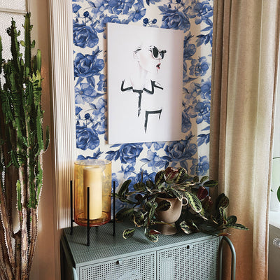 Tempaper's Forget-Me-Not Peel And Stick Wallpaper By Alice + Olivia shown above a plant and candle behind a picture frame.
