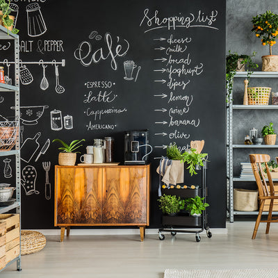 A kitchen area with lots of plants and Tempaper's chalkboard wallpaper with a shopping list, cafe offering, and more kitchen designs drawn on it.