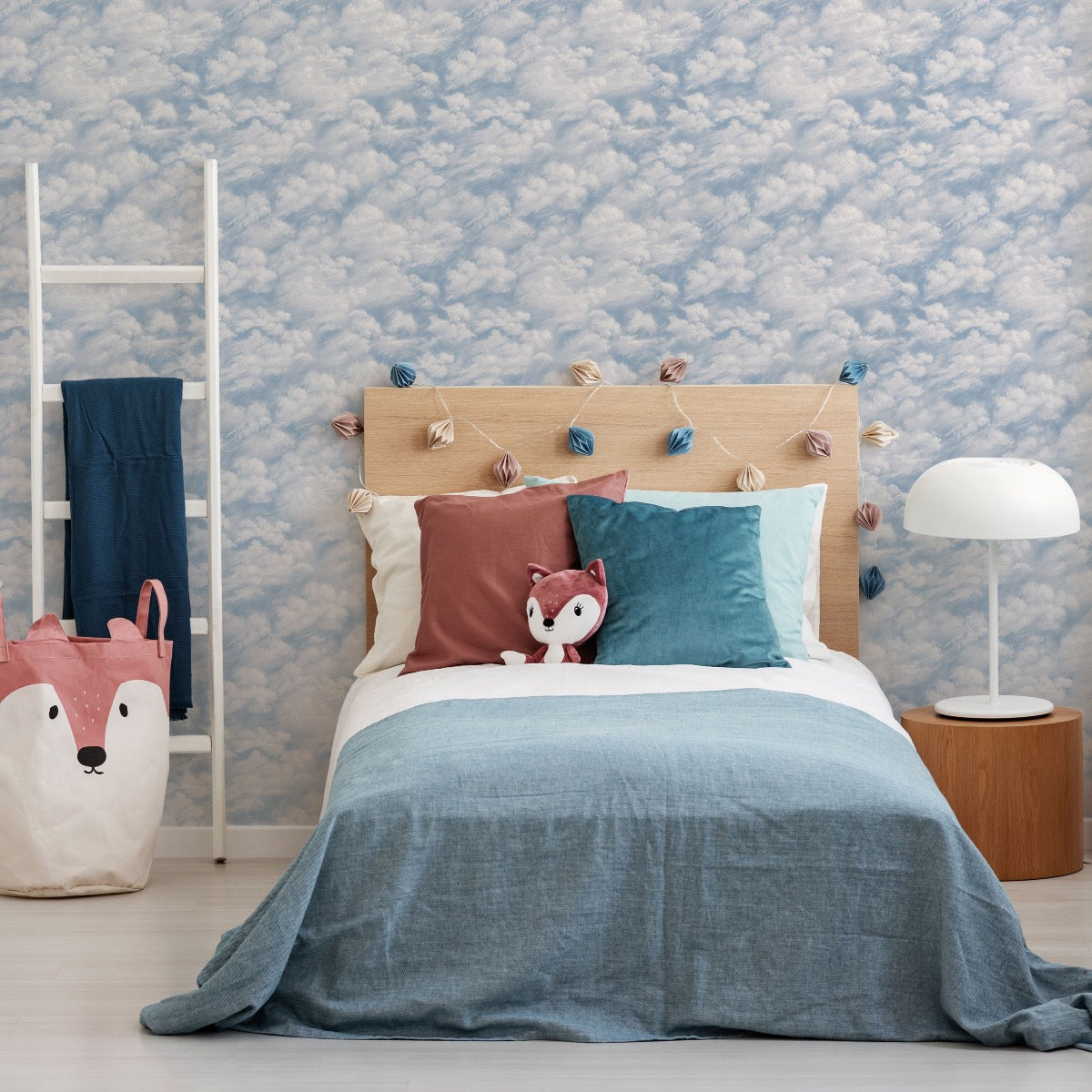 Tempaper's Clouds Peel And Stick Wall Mural in light blue shown in a kids bedroom behind a bed.