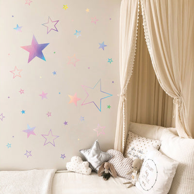 A wall in a girl's bedroom with a white canopy and holographic Star wall decals from Tempaper.