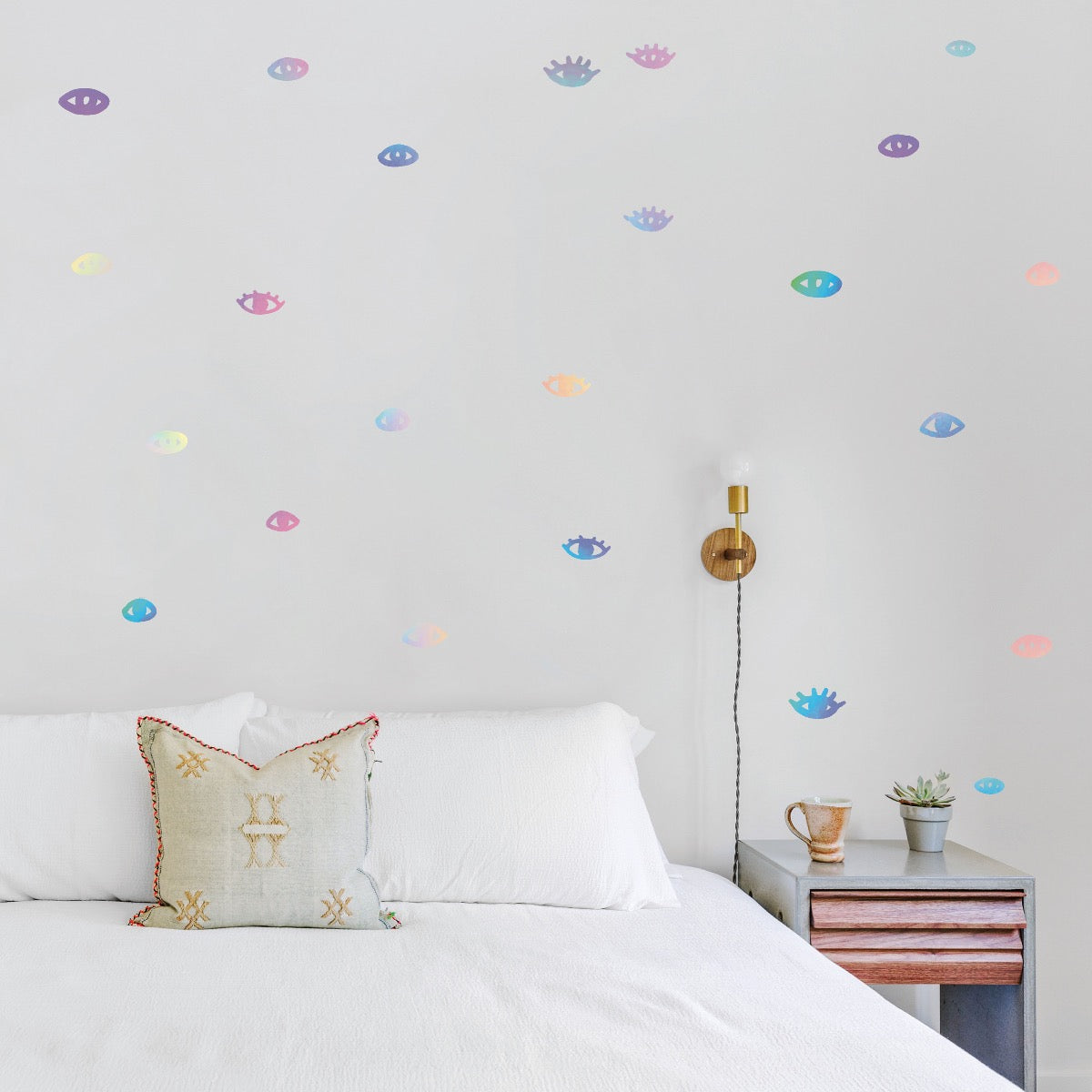 Tempaper's holographic You Are Seen wall decals placed on the wall in a bedroom with a white bed. 