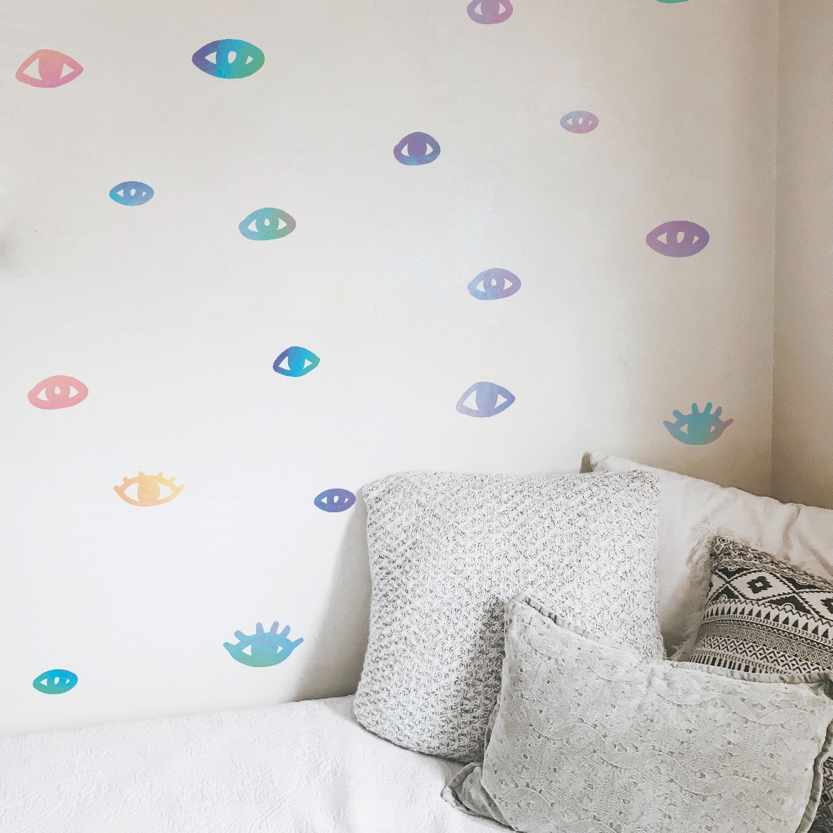 An upclose look at the holographic You Are Seen wall decals from Tempaper placed on a white wall next to a white bed.