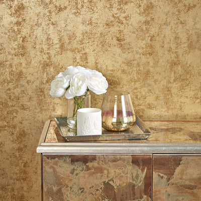 Tempaper's Distressed Gold Leaf Peel And Stick Wallpaper in metallic gold shown behind a sideboard and a plant.#color_gold-leaf
