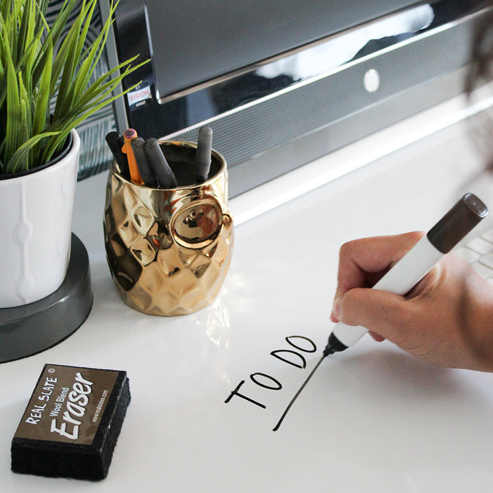 Tempaper's Dry Erase Peel And Stick Wallpaper shown on a desk with a person writing on it.