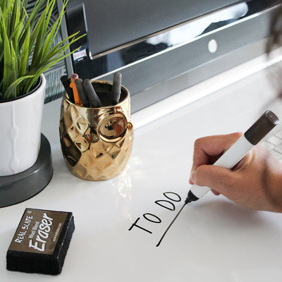 Tempaper's Dry Erase Peel And Stick Wallpaper shown on a desk with a person writing on it.