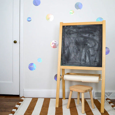 A child's art easel standing in front a wall decorated with holographic Dots wall decal from Tempaper.