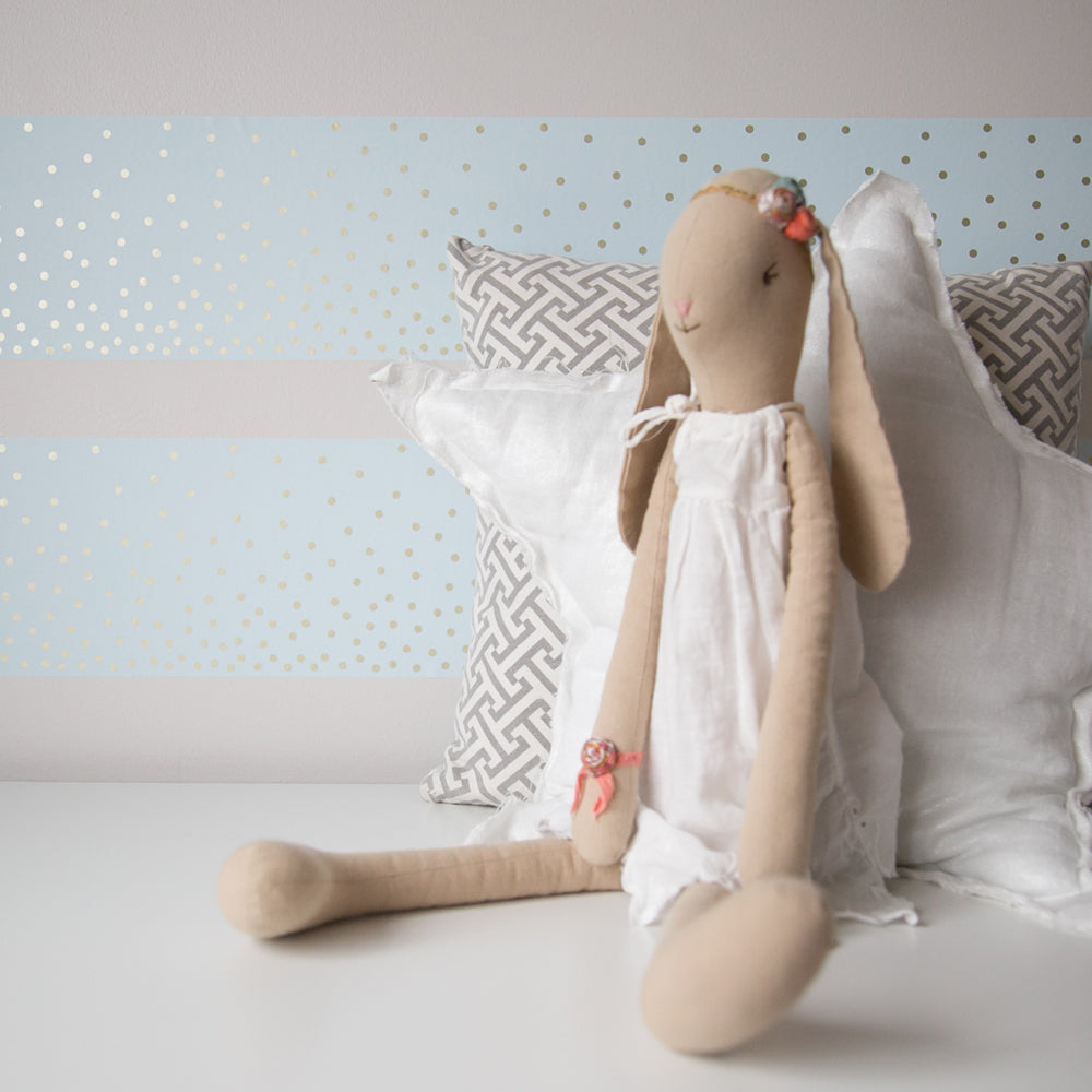 Tempaper's Falling Dots Border Peel And Stick Wallpaper shown behind a doll and pillows.