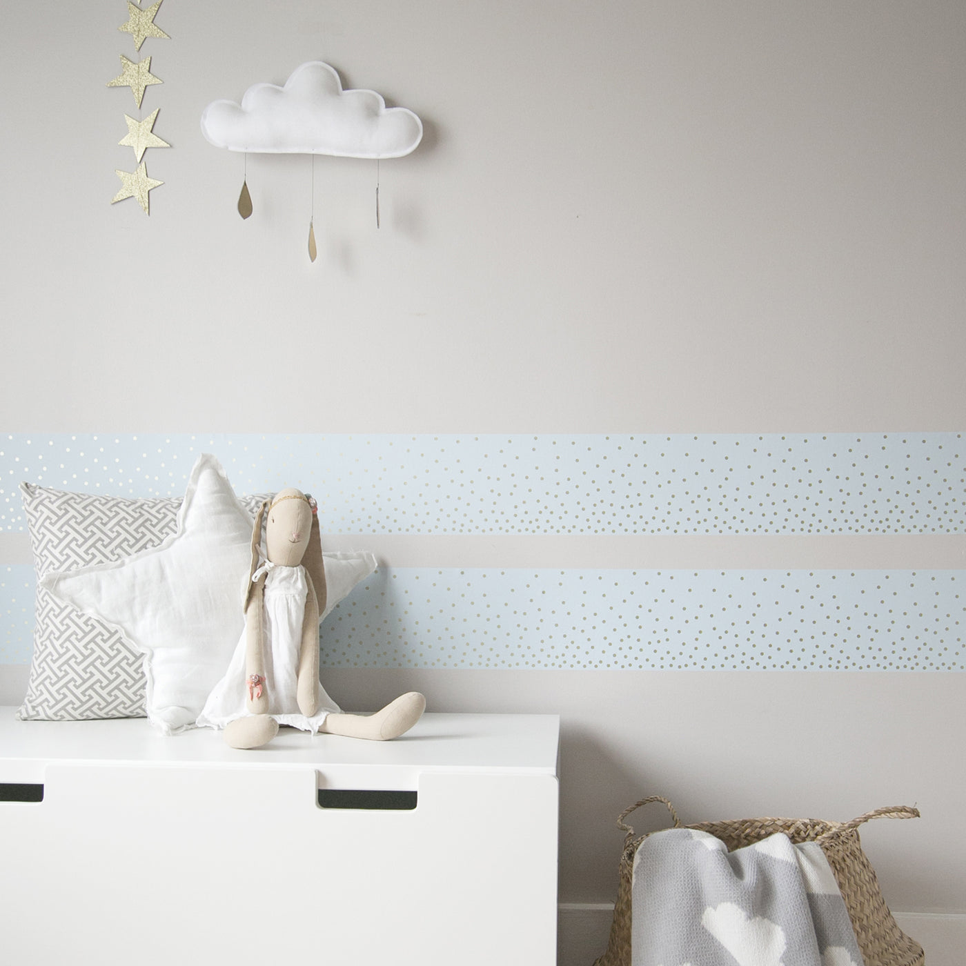 Tempaper's Falling Dots Border Peel And Stick Wallpaper shown above a chest behind a doll and pillows.