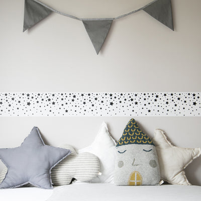 Tempaper's Falling Stars Border Peel And Stick Wallpaper in black and white shown in a bedroom above a bed.