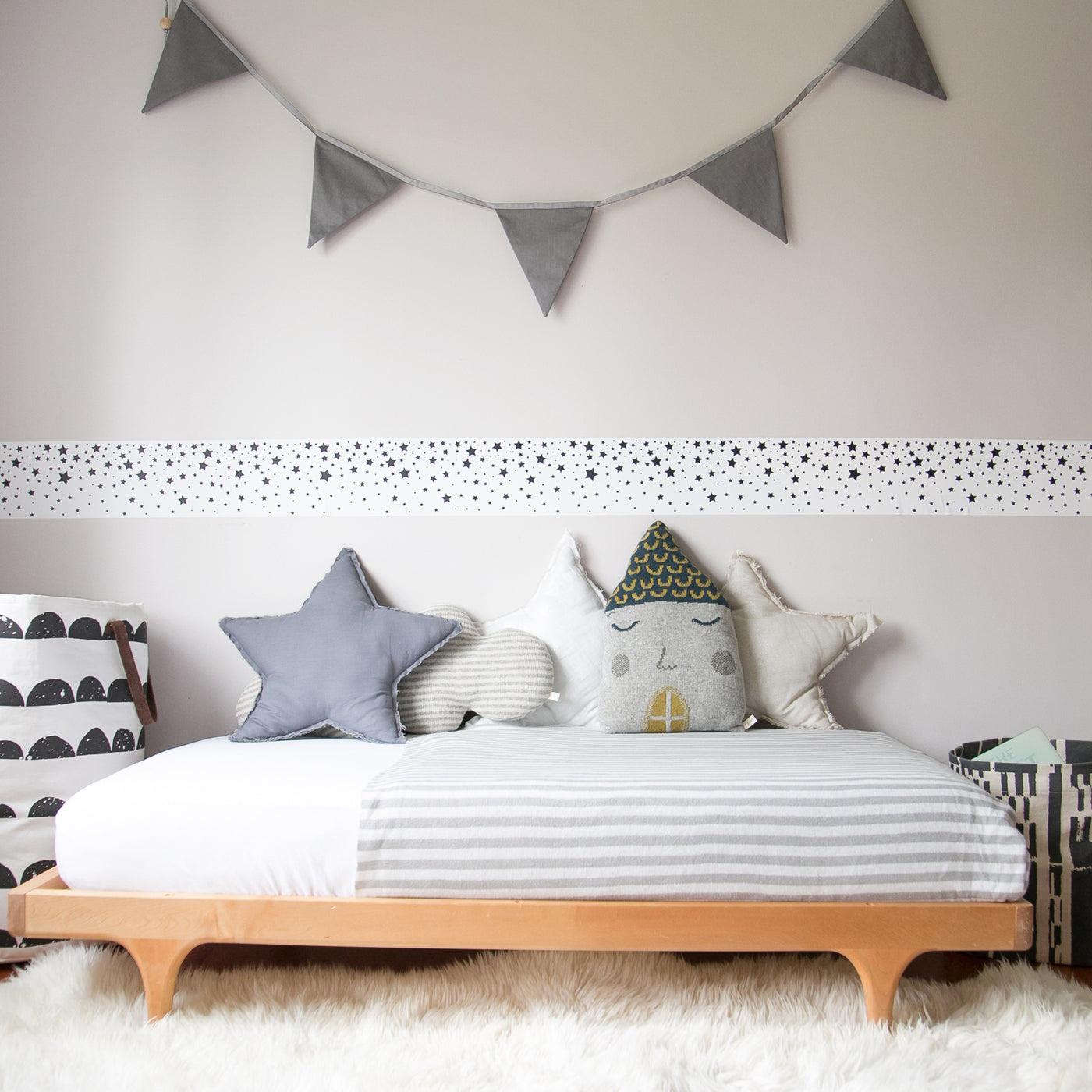 A strip of Tempaper's Falling Stars Border Peel And Stick Wallpaper in black and white shown above a bed in a bedroom.