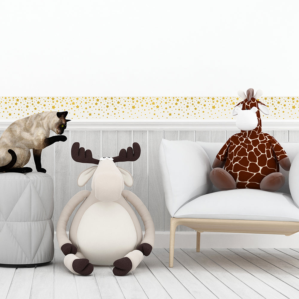 Tempaper's Falling Stars Border Peel And Stick Wallpaper in white and gold shown in a kids bedroom behind dolls and a chair.