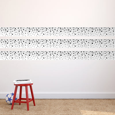 Strips of Tempaper's Falling Stars Border Peel And Stick Wallpaper in black and white shown above a stool.