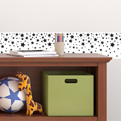 Tempaper's Falling Stars Border Peel And Stick Wallpaper in black and white shown above a bookcase.
