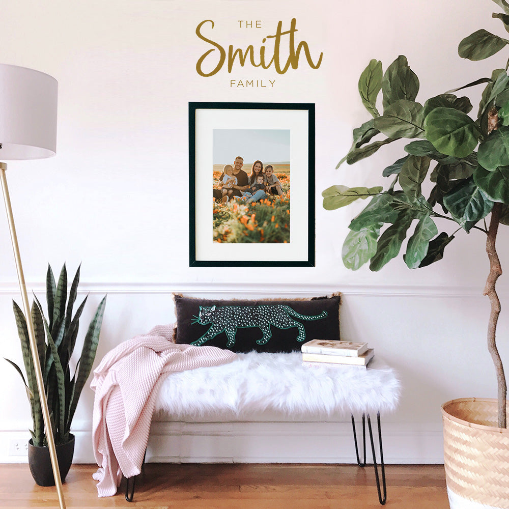 An up close view of Tempaper's Custom Family Name Wall Decal with "The Smith Family" as an example shown above a picture frame and bed.