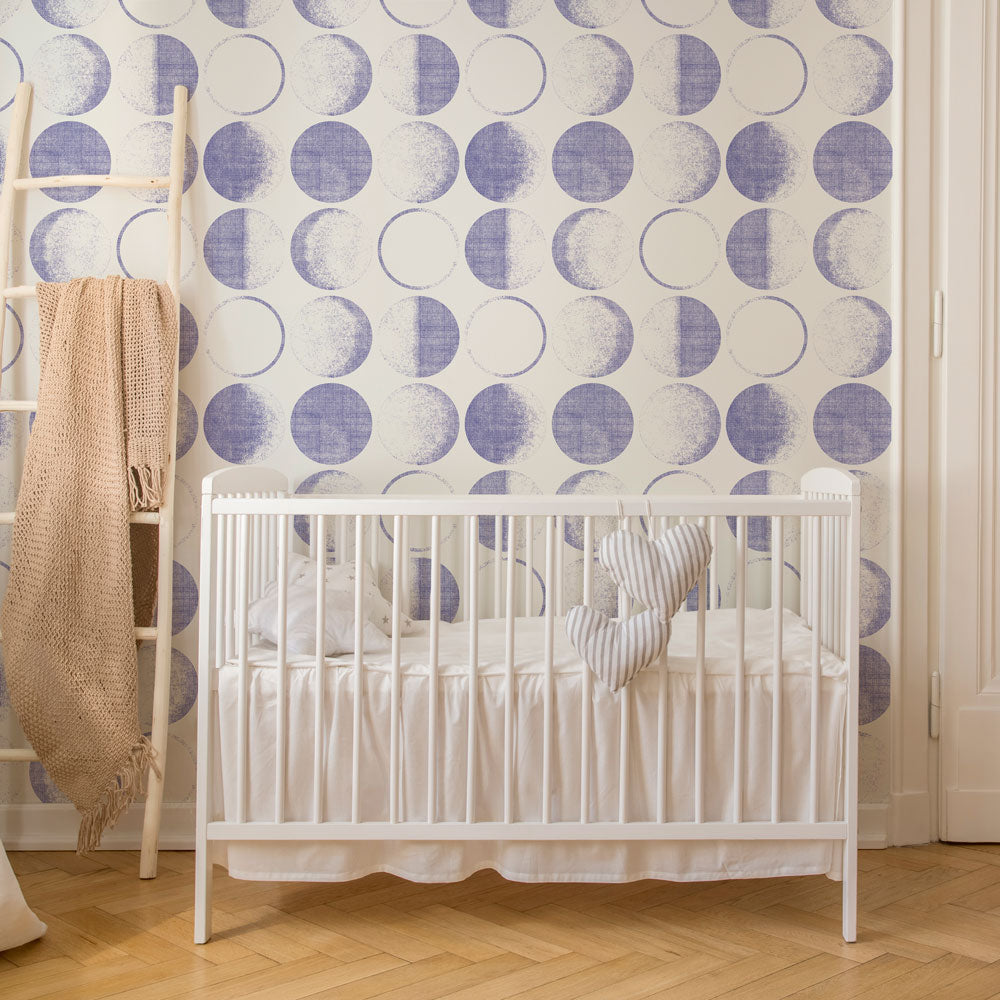 Tempaper's Moons Peel And Stick Wallpaper in a periwinkle colorway in a kids bedroom with a white crib.