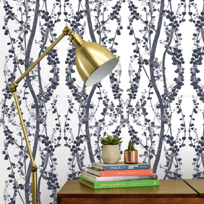 Branches WALLPAPER in navy blue behind a table and lamp.