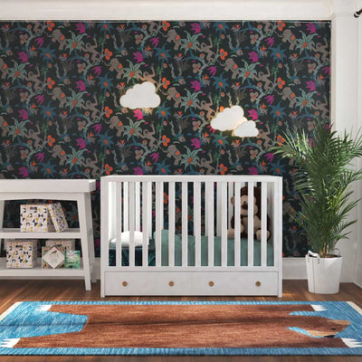 A nursery with a white crib and changing table, a tall palm plant, a rug with a stretched out bear, and Tempaper's passion fruit Monkey Business removable wallpaper accenting the wall behind the crib. #color_passion-fruit