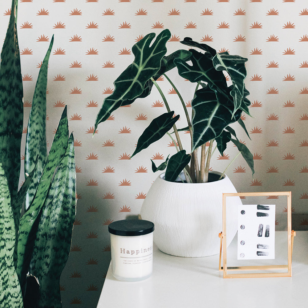 Two plants and a white table in front of Tempaper's Sunbeam Peel And Stick Wallpaper.
